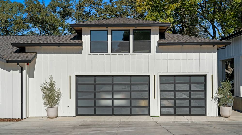 A white house finished in vertical board-and-batten siding, with dark glass garage doors and black-framed windows