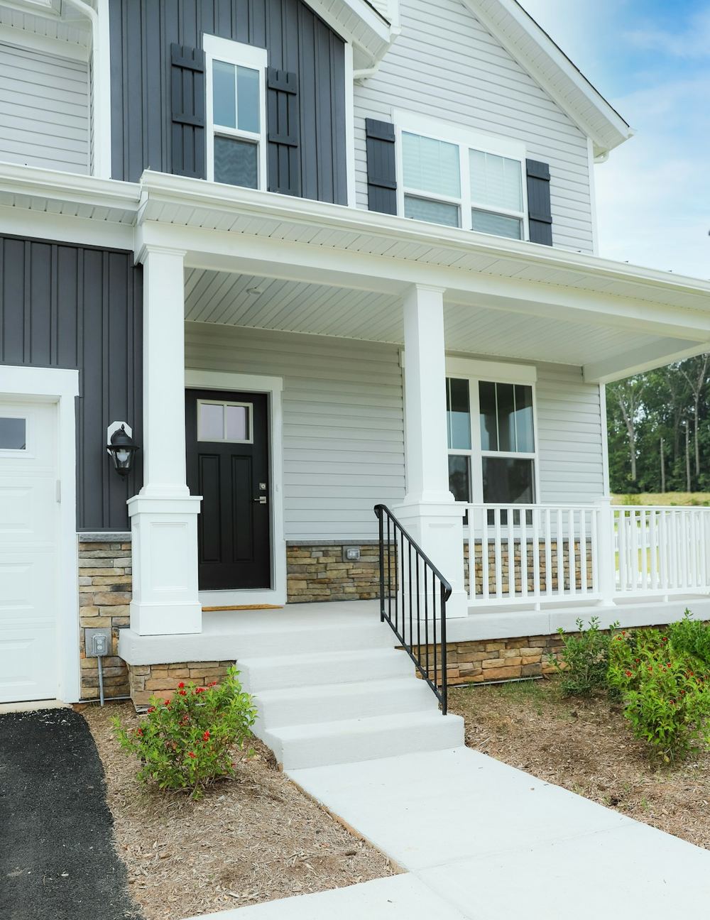 A new two-story home with white horizontal vinyl siding below and dark vertical board-and-batten siding above the porch