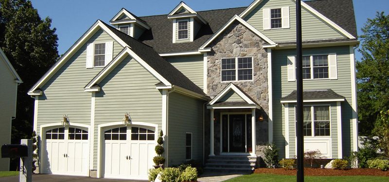 A two-story house with sage-green lap siding, white trim and a stone-faced entry