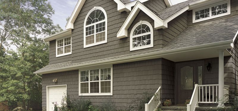 A gray two-story house with shake-style siding, white trim and arched windows in its gables